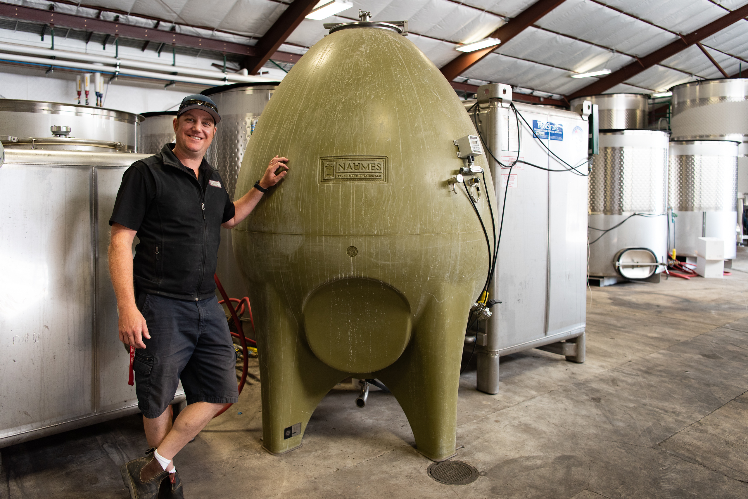 Winemaker Chris Graves stands smiling next to a specialized ceramic fermentation container shaped like an enormous green egg.